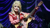 Dolly Parton 2022 mit Gitarre auf einer Bühne.
