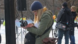 Junge Frau mit Kamera in der Hand und Schreibblock unter dem Arm