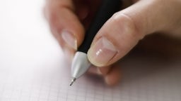 Eine Hand schreibt mit einem Stift auf einem Zettel