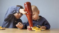 Zwei Kinder essen Pommes Frites mit Ketchup und tragen blau gestreifte Hemden im Partnerlook
