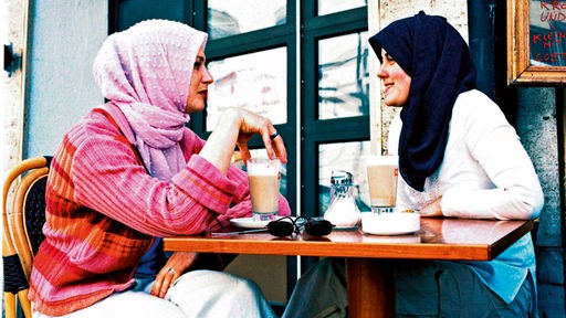  Junge Musliminnen in modischer Kleidung und Kopftüchern sitzen in einem Straßencafe in München