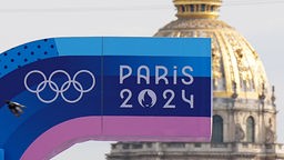 Eine Anzeigetafel mit dem Logo der Spiele und die Olympischen Ringe sind vor der Kuppel des Invalidendoms zu sehen.