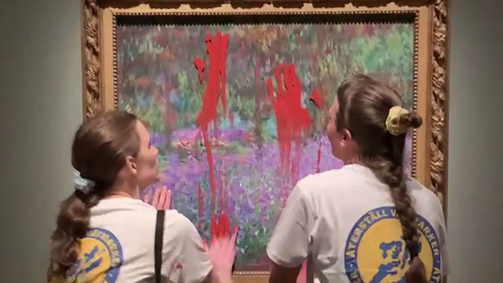 Zwei Frauen vor einem Monet-Gemälde, das sie mit ihren Händen mit roter Farbe beschmieren.