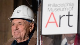 Aufnahme von 2017: Der Architekt Frank Gehry mit einem weißen Bau-Helm neben einem Wimpel mit der Aufschrift "Philadelphia Museum of Art".