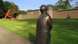 Die Bronzestatue eines Mannes ziert einen der Gehwege um das Kröller-Müller-Museum. Großflächig ist Rasen angelegt, freundliche Parkfläche und Raum für Outdoor-Skulpturen.