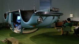 eine Installation, die aus einem hellblauen, umgedrehten alten VW-Käfer ohne Räder besteht, innen ein Video-Screen