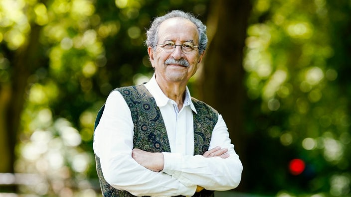 Der Schriftsteller Rafik Schami steht in einem Park.