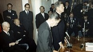 Gründungsveranstaltung des Deutschen Entwicklungsdienstes, John F. Kennedy (r. stehend), Bundespräsident Heinrich Lübke (l. sitzend) und Bundeskanzler Konrad Adenauer (2. v. r.)
