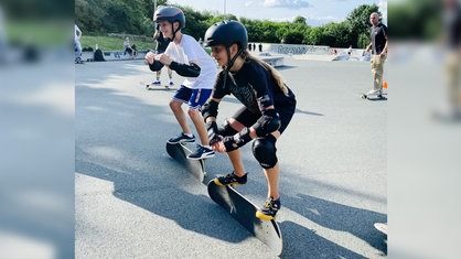 Jugendliche stehen in Schutzkleidung auf ihren Skateboards