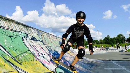 Ein Mädchen in Schutzkleidung auf dem Skateboard in einer Halfpipe