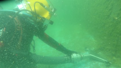 Ein Taucher arbeitet unter Wasser mit einem Staubsauger