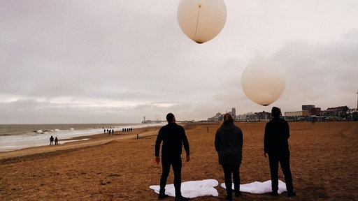 Bestatter lassen Ballons mit der Asche eines Verstorbenen am Strand aufsteigen.