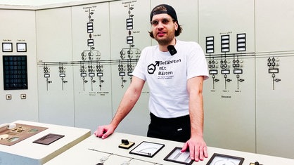 Ein junger Mann mit Kappe und einem weißen T-Shirt mit der Aufschrift "Gefährten mit Bärten" lehnt an einem Tisch