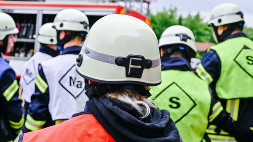 Mehrere Kinder in Warnwesten und Helmen. Sie stehen mit dem Rücken zur Kamera.