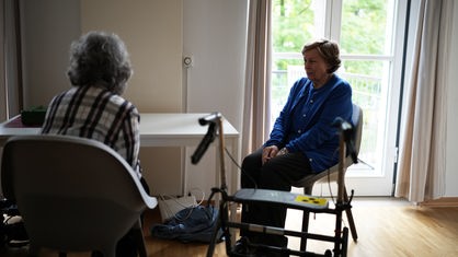 Zwei Frauen sitzen auf Stühlen an einem Tisch. 