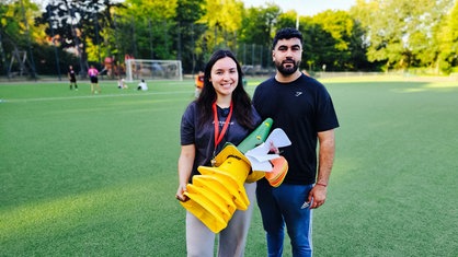 Carolina Graef Alarcón und ihr Co-Trainer Abdulrahman Mohamad Anz stehen auf dem Fußballplatz, Graef Alarcón trägt Pylonen