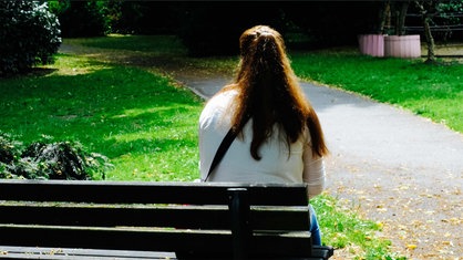 Sandra Riesener, eine Frau mit braunen langen Haaren, sitzt auf einer Bank