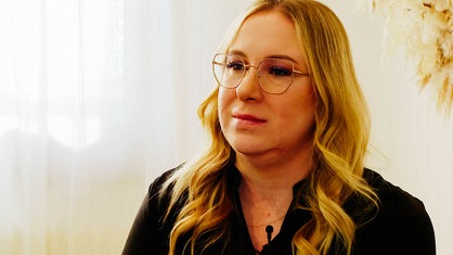 Eine Frau mit langen blonden Haaren und Brille schaut in die Kamera.