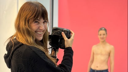 Eine Fotografin in ihrem Fotostudio, sie fotografiert eine oberkörperfreie Frau