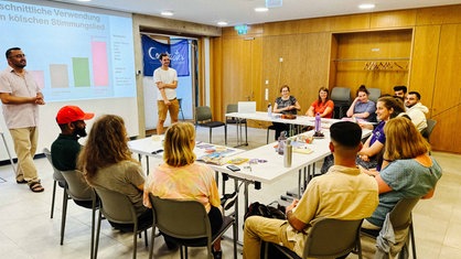 Pascal Bittner und Rahmi Damir stehen vor einer Gruppe sitzender Schüler und Schülerinnen und geben eine Präsenation. 