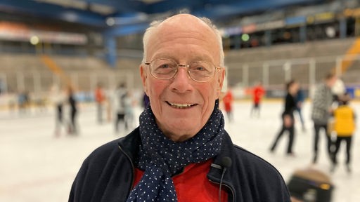 Dieter Büllesbach steht im Eisstadion neben dem Eis und lächelt in die Kamera.