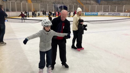 Ein älterer Mann bringt einem Kind Eislaufen bei