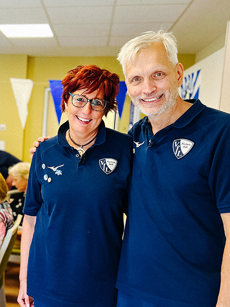 Gaby und Christian Sonnek im VfL-Trikot mit Senioren im Hintergrund.