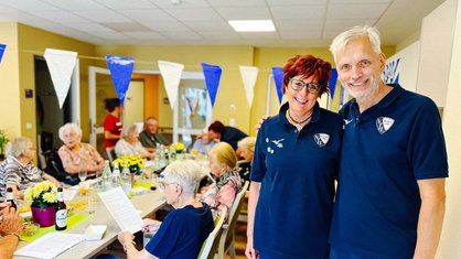 Gaby und Christian Sonnek im VfL-Trikot mit Senioren im Hintergrund.