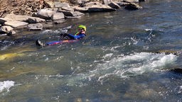 Ein Strömungsretter schwimmt mit Schutzkleidung in einem Fluss