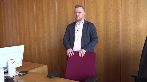 Dominik Pinsdorf steht hinter seinem Stuhl am Richtertisch