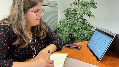 Angelika Voge sitzt vor einem Tablet und hat Kopfhörer im Ohr