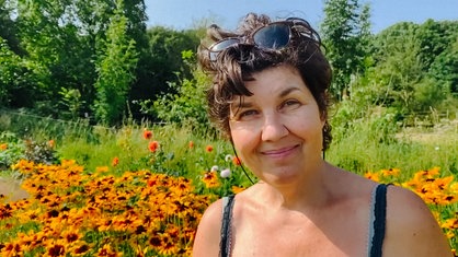 Eine Frau mit braunen Haaren steht vor einer Blumenwiese