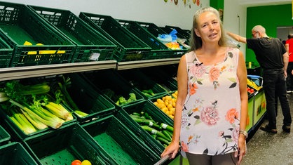 Eine Frau posiert vor Obst- und Gemüsekästen.