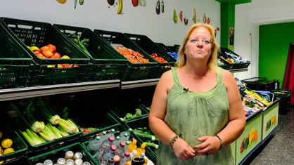 Eine Frau posiert vor Kisten voller Gemüse und Kartoffeln.