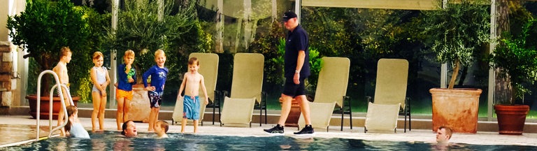 Ein Mann und mehrere Kinder stehen an einem Schwimmbeckenrand. 