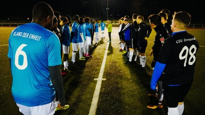 Zwei Fußballmannschaften stehen sich auf dem Spielfeld zu Spielbeginn gegenüber