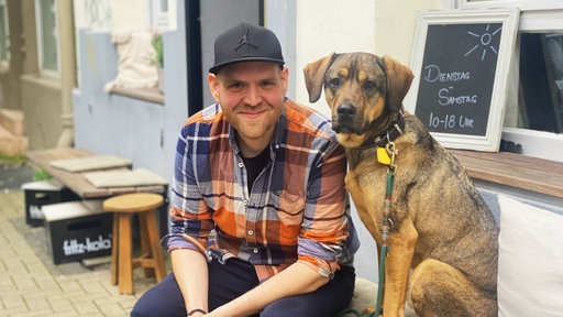 Ein Mann sitzt auf einem Stuhl. Neben ihm sitzt ein Hund.