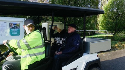 Ein Mann in einer gelben Jacke fährt ein älteres Paar in einer Art Golfcart 