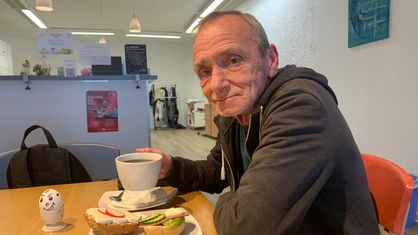 Ein Mann beim frühstücken, in seiner Hand hält er eine Tasse Kaffee.