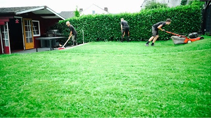 Drei Jungs beim Rasenmähen und Hecke schneiden