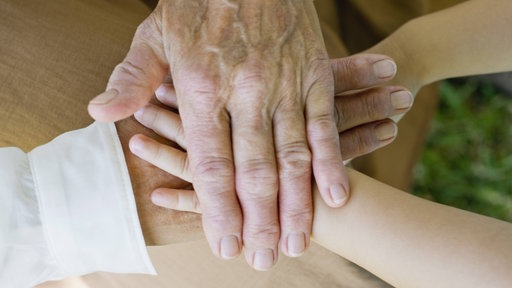 Die Hand einer Seniorin hält die Hand eines kleinen Kindes