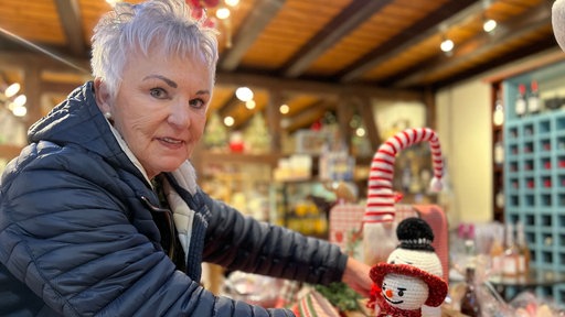 Eine Frau mit grauen Haaren stellt einen kleinen, weißen, gehäkelten Schneemann auf ein Regal