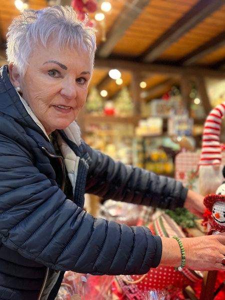 Eine Frau mit grauen Haaren stellt einen kleinen, weißen, gehäkelten Schneemann auf ein Regal