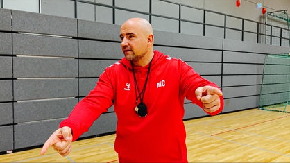 Maik Cohrs trägt einen roten Pullover und gestikuliert beim Handballtraining mit den Armen. 