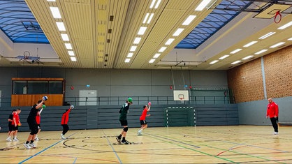 Jugendliche trainieren in einer Sporthalle Handball.