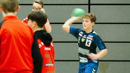 Noah Cohrs im blauen Handballtrikot wirft einen grünen Handball