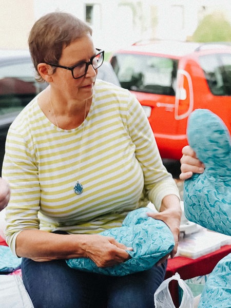 Uschi Hellmich sitzt zusammen mit zwei weiteren Frauen, die neue Herzkissen nähen und befüllen.