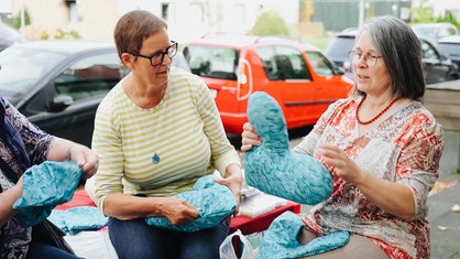 Uschi Hellmich sitzt zusammen mit zwei weiteren Frauen, die neue Herzkissen nähen und befüllen.