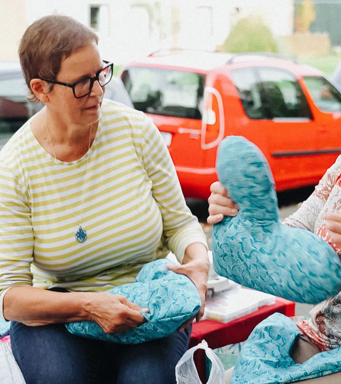 Uschi Hellmich sitzt zusammen mit zwei weiteren Frauen, die neue Herzkissen nähen und befüllen.