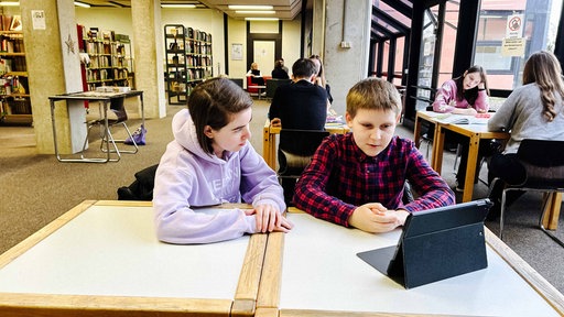 Eine Jugendliche Nachhilfelehrerin sitzt neben einem ihrer Schüler an einem Tisch der Bibliothek in Kerpen.